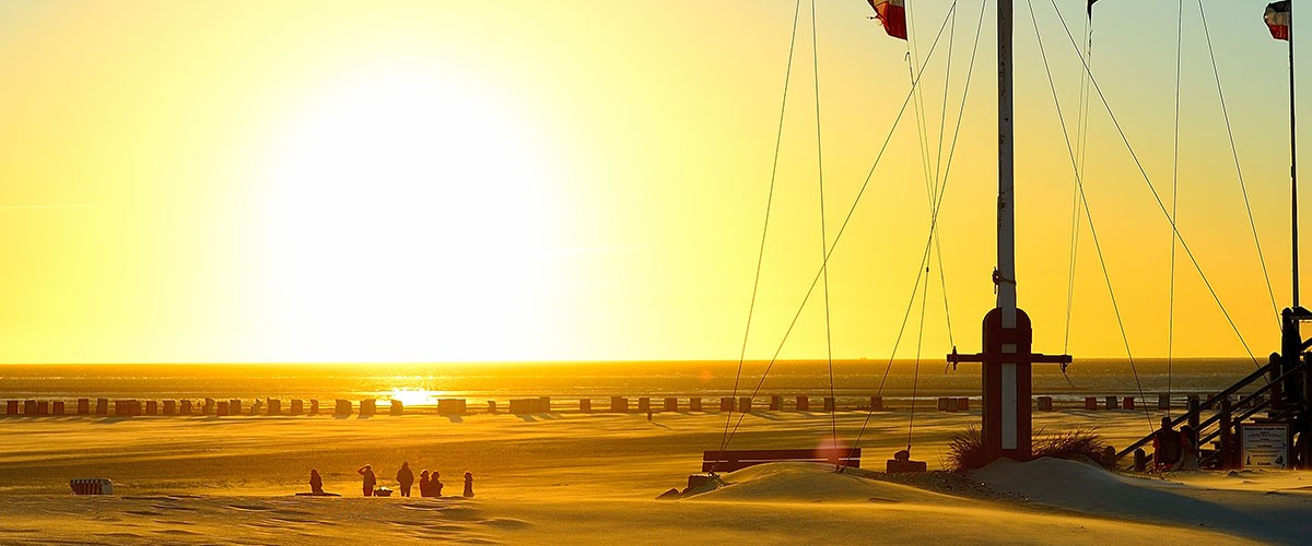 Abendsonne über dem Strand hinter einem Mast mit Tauwerk