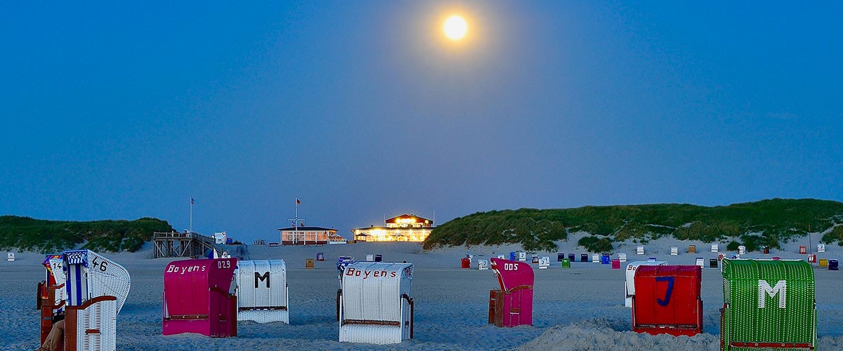 Bunte Strandkörbe am Abend, darüber der aufgehende Mond