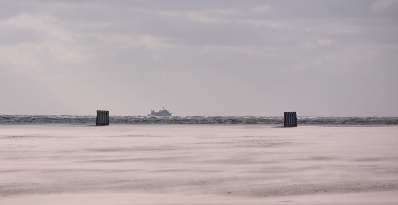 Weiter Strand mit Strandkörben, am Horizont die Fähre
